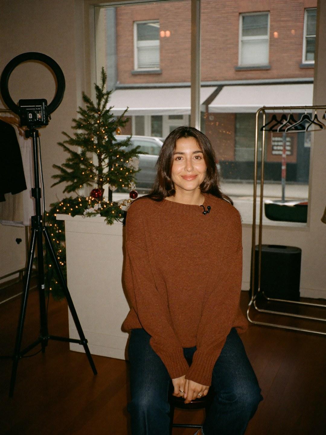 A live selling host beside a ring light in a boutique decorated with a lit garland and red baubles.