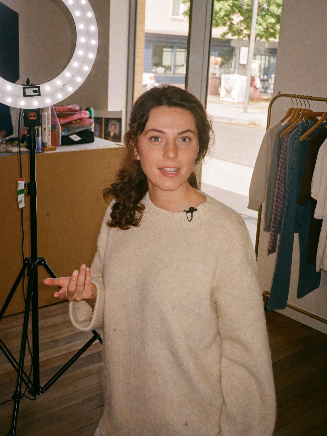 A live selling host beside a lit ring light in a boutique, mid-sentence to camera.